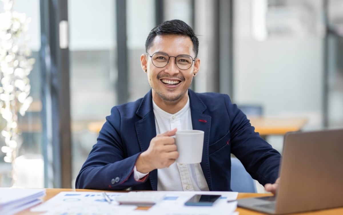 A young man working at a laptop holding a cup of coffee, property management virtual assistant concept