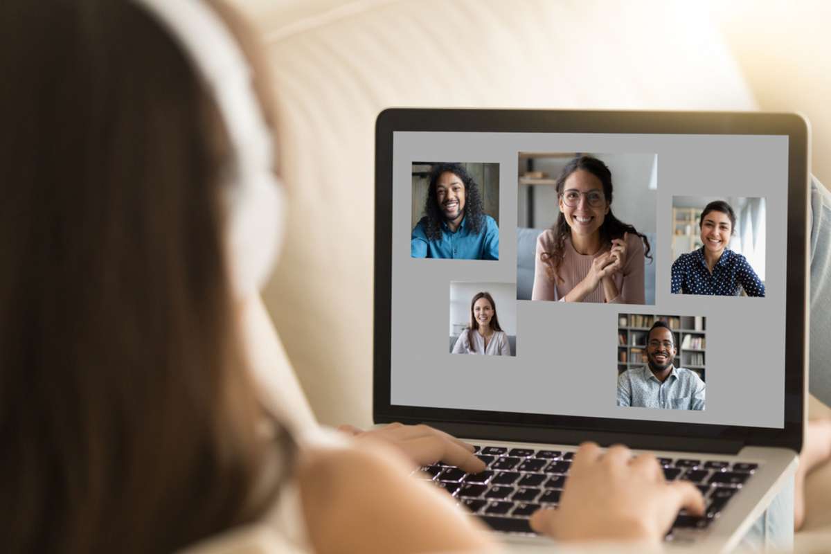 Back view of young female sit rest on sofa ta home talk chat online on video call on laptop with diverse friends