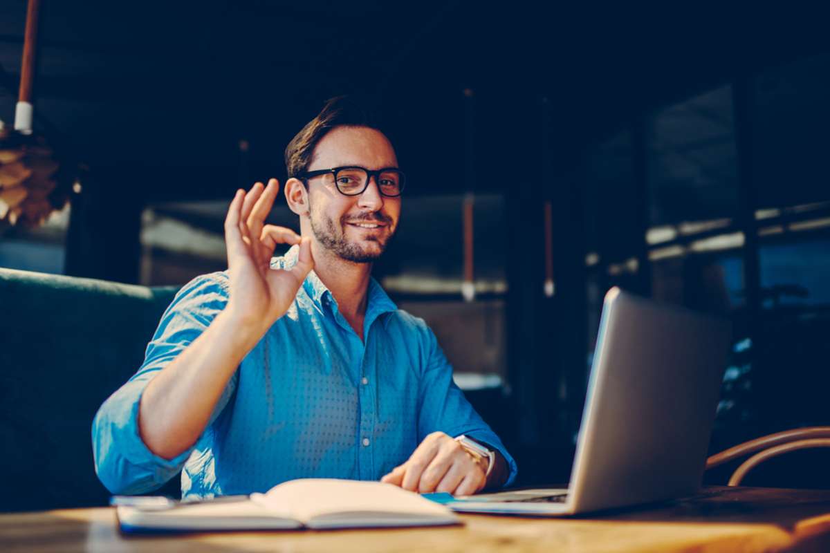 Portrait of skilled male freelancer showing ok sign completing working on project satisfied with salary