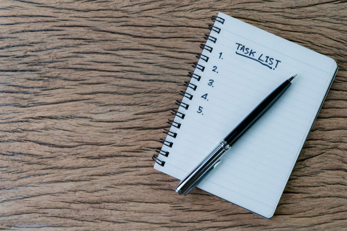 Task checklist in project management concept, pen on white paper notepad with handwritten headline as Task List and numbers listed on wood table,