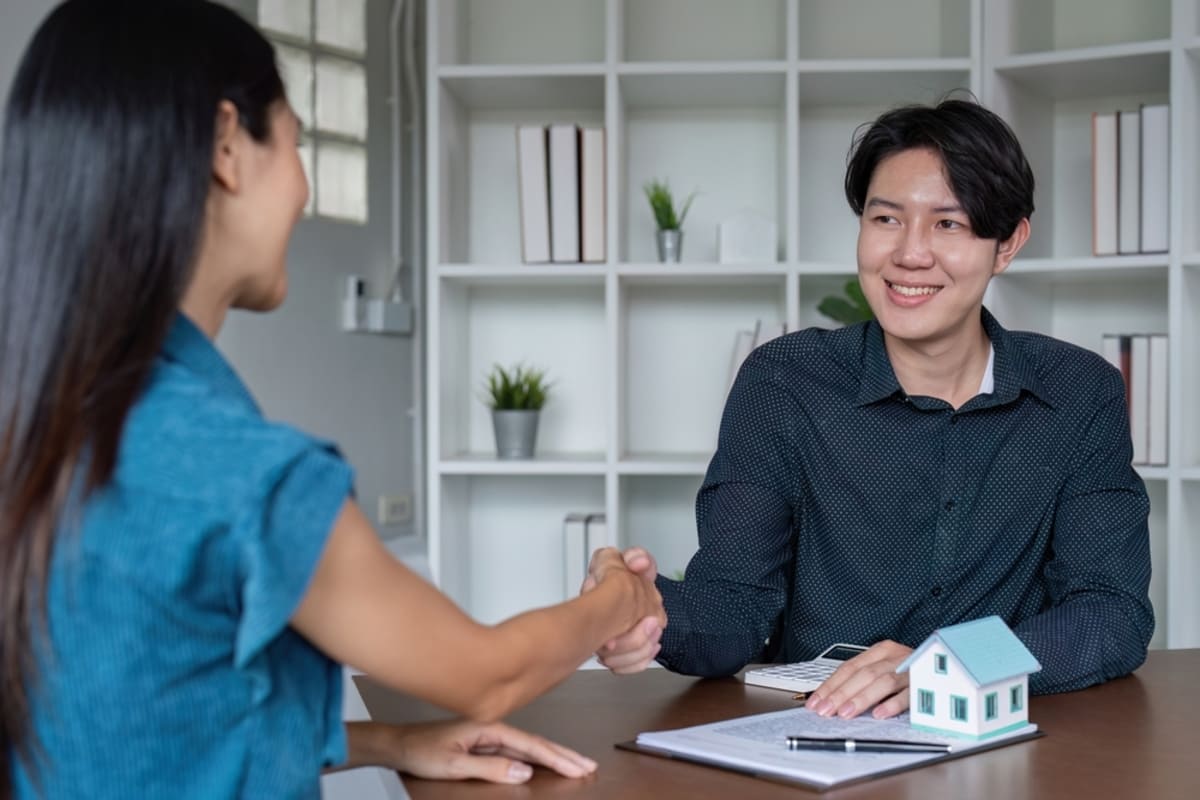 Two people shaking hands next to a model home