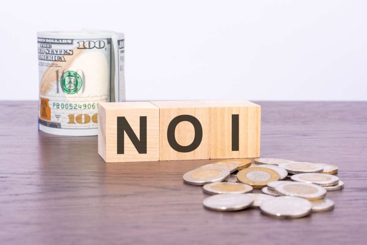 top view of wooden blocks with text NOI (Net Operating Income) over US dollar banknotes on a brown background. business concept